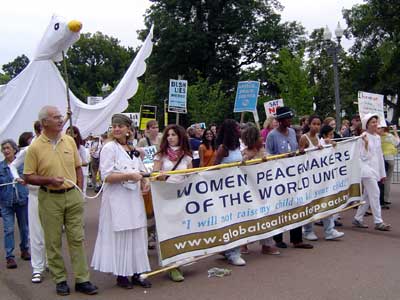 Women of all ages and ethnicities carry a banner that says "Women peacemakers of the world unite".